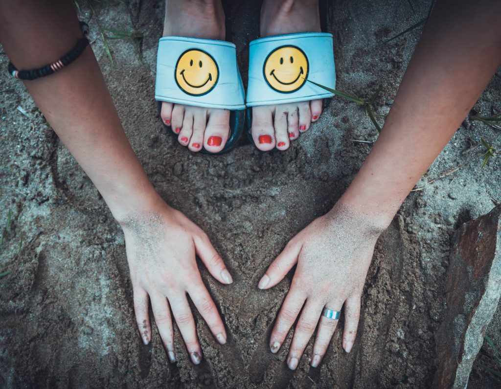 Woman's hands in the sand wearing happy face sandals