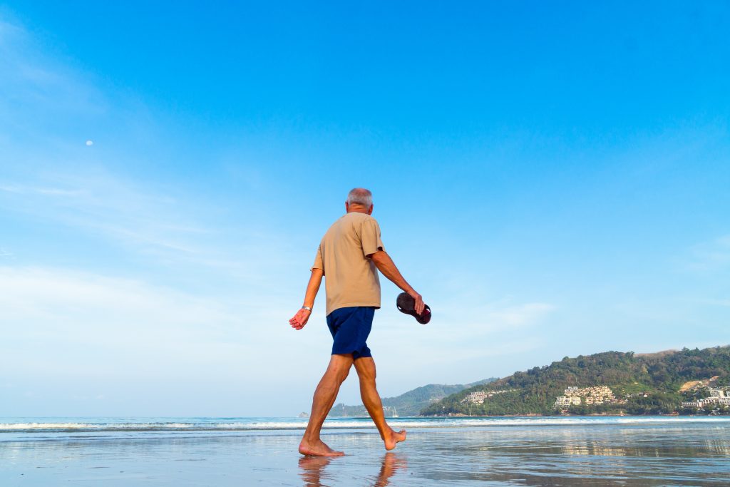 older man walking barefoot along a beach